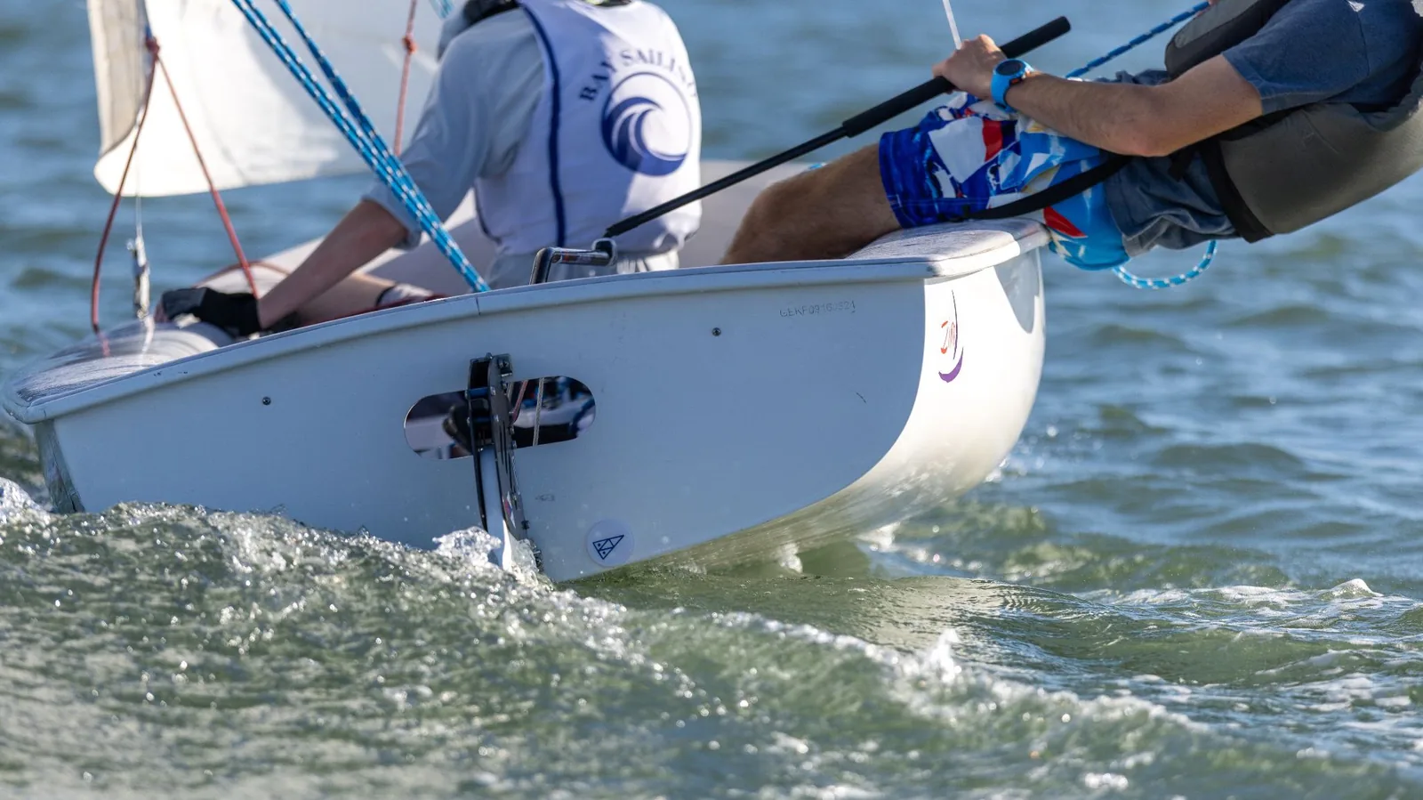 A sailor hiking out over the side of an FJ, with the transom and drain plug in view.